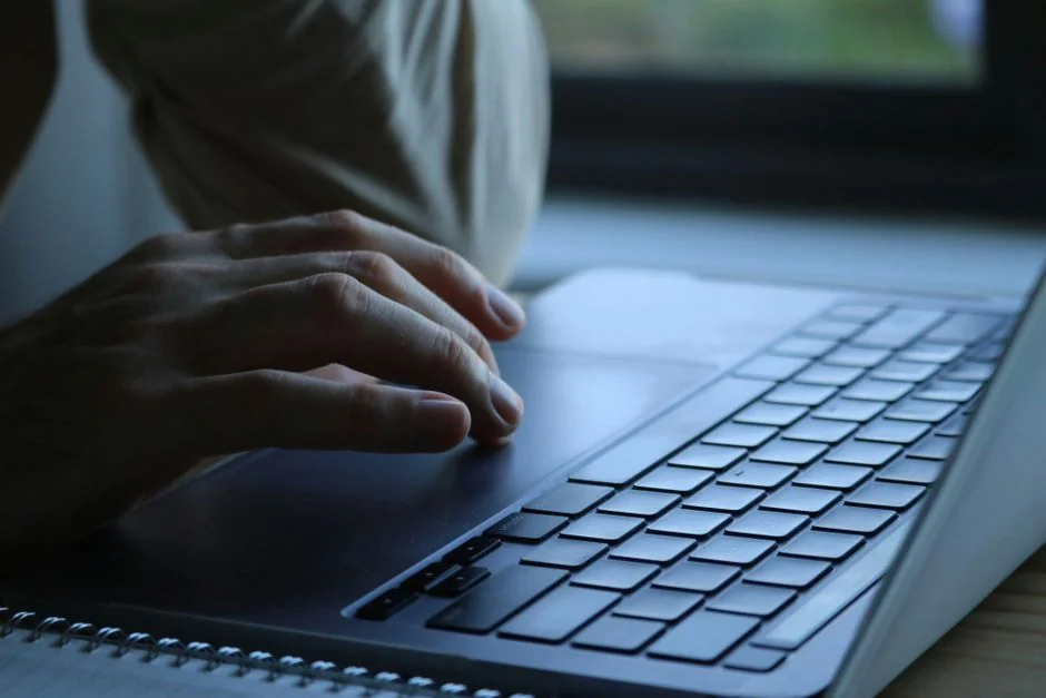 Man analyzing stock trends with laptop and mobile trading app at a modern workspace.